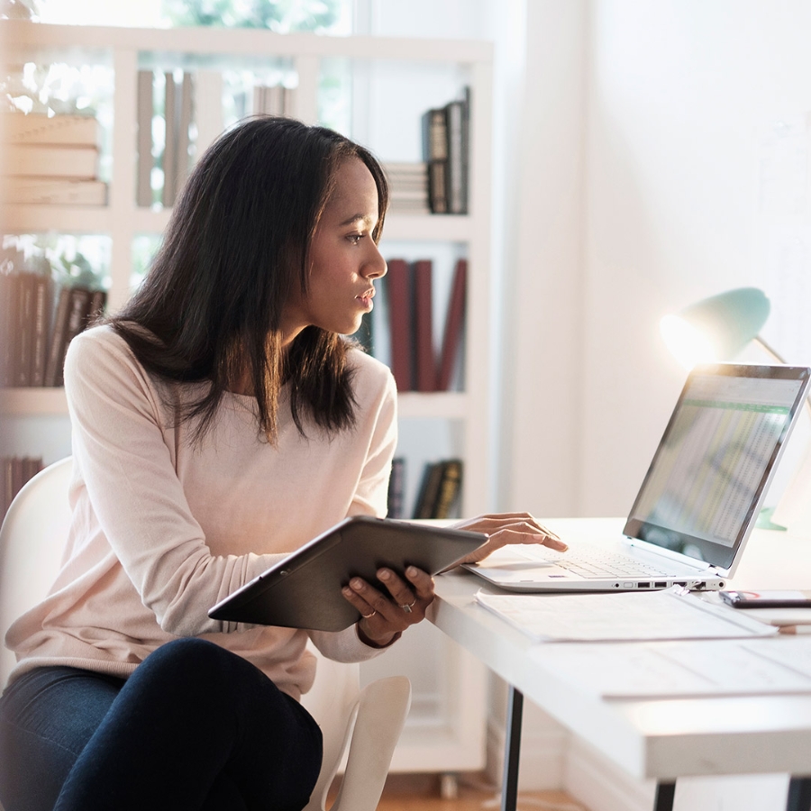 A woman sitting on desk and working on her laptop in home office