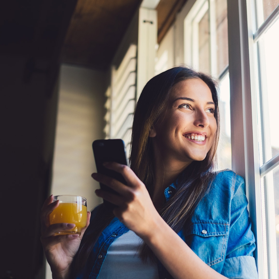 smiling young lady looking outside the window while holding smartphone