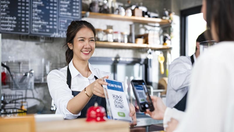 Female Barista or cashier receving paying from customer via smart phone at a coffee shop counter