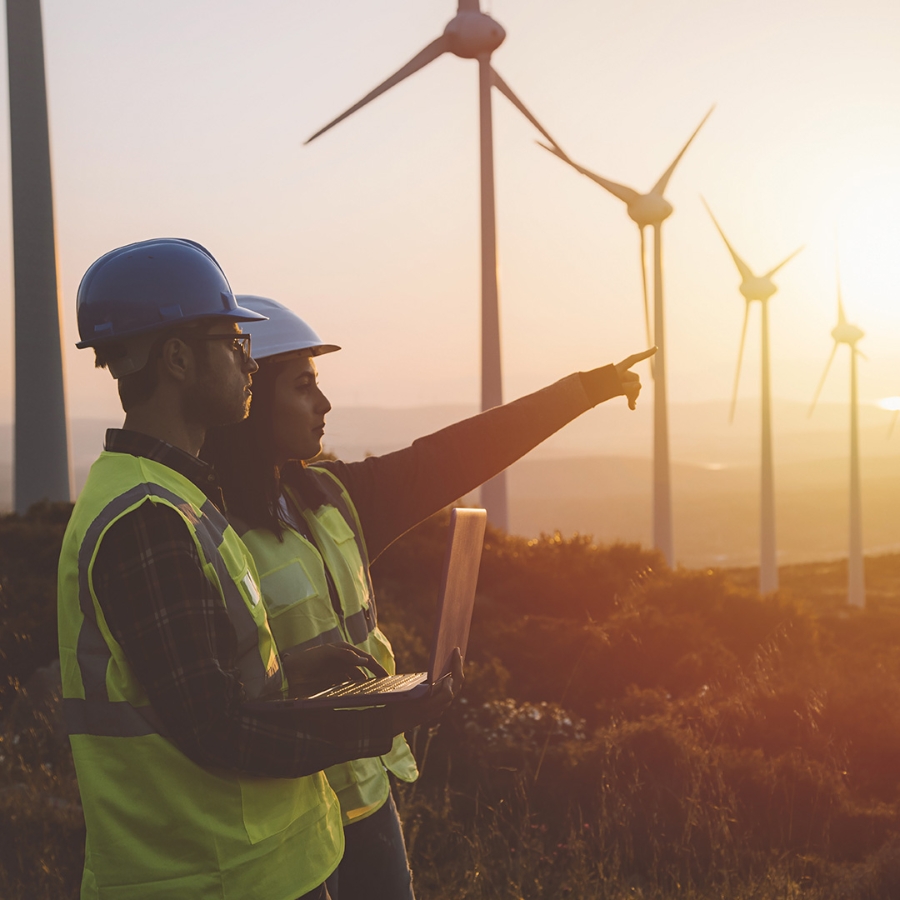 two engineers with a laptop standing in front of wind turbines