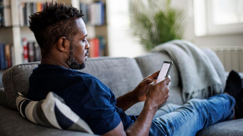 Man sitting on couch and sending text message on phone