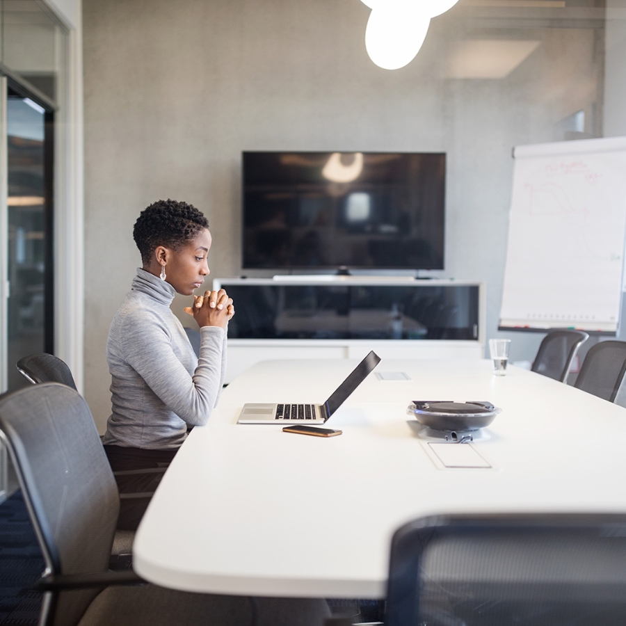 A woman sitting alone in a meeting room and working on her laptop