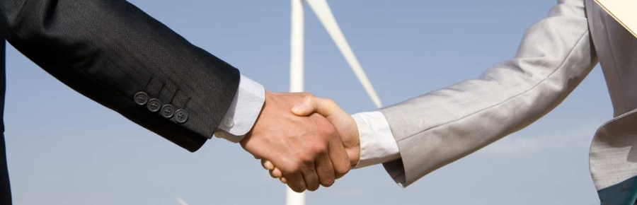 Two men shaking hands in front of a wind turbine